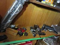 Wide shot showing vintage Kodak camera in brown case, assorted pocket cameras, camera attachments, and black camera bag on wooden shelf