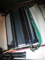 Full view of the black button accordion on its case, showing the bellows, buttons, and straps.