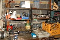 Full view of work table with various tools including the Black and Decker power saw in yellow crate, oil can, hand tools, and other workshop items.