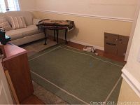 Green area rug with light border placed on hardwood floor and carpet beneath one side