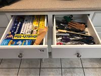 Two kitchen drawers open showing kitchen utensils in one and food wraps in another.