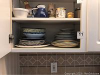 Photo showing cupboard with stacked assorted plates in multiple designs and a few pitchers and canisters on top shelf.
