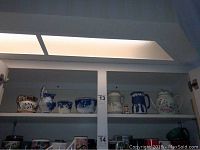 Upper shelf of cabinet showing Wedgewood blue imprint pitcher, tea canister, sugar creamer bowl among other ceramics