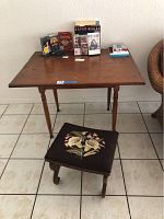 Full view of antique wooden table with several DVDs on top and antique foot stool in front.