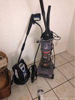 Hoover upright vacuum cleaner with hose and power cord, standing on tile floor.