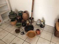 Collection of various ceramic pots, vases, bowls, and a duck figurine placed on tiled floor near a wall, showcasing variety and sizes.