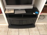 Front view of black TV stand with open shelf and flat top surface, holding a TV base.