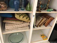 Shelving unit with beige quilted pillows, striped pillows, embroidered pillows, vases and decor items.