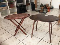 Two small tables side by side, one folding wooden tray table with crossed legs and one round wooden beverage cart table with four legs.
