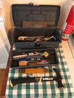 Overall view of open toolbox showing two trays of hand tools including pliers, scissors, screwdrivers, measuring tape, and brushes, plus claw hammer and First Alert fire extinguisher beside it.
