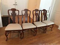 Four wooden dining chairs lined up, showing front view with striped cushions and carved backs on hardwood floor.