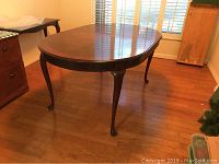 Full view of the wood dining table showing the polished, dark wood oval top and curved legs