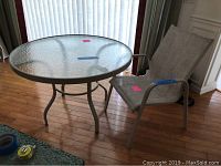 Glass top round table with aluminum frame and legs, 42.5 inches diameter, shown indoors with wooden floor background.