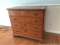 Front view of vintage wood dresser showing four drawers with decorative brass hardware and some veneer damage on top drawer face and top surface.