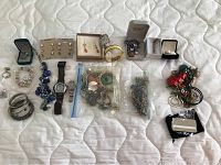 Full view of costume jewelry lot spread on quilted white surface including bracelets, necklaces, earrings, and watches.