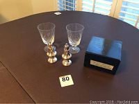 Full lot showing pair of silver salt and pepper shakers, two wine glasses and a small black box on a dark table surface.