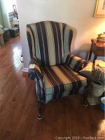 Wing back chair with vertical striped upholstery and wooden legs shown in full view