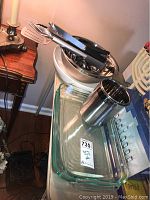 Set of BBQ tools with black handles inside two stainless steel bowls, rectangular clear Pyrex baking dish below with a metal cup.