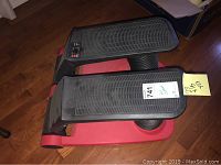 Full view of the air climber exerciser showing the two black textured foot pedals and red base.