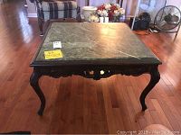 Full view of square accent table with green marble top and carved wooden legs on a hardwood floor.