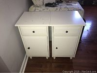 Two white wooden end tables positioned side by side, showing overall condition and visible damage on one table's top.