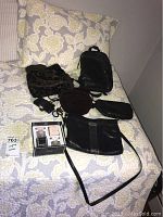 Photo of various purses arranged on a bed with a floral pillow background, including black leather, black velour, and dark brown velour purses.