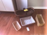 Four wicker baskets of different sizes and styles arranged on floor near white cabinet, showing overall lot contents
