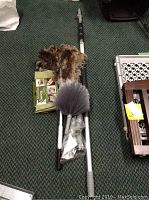 Lot contents showing ostrich duster, gray feather duster head, microfiber cloths, and bulb changer parts arranged on green carpet.