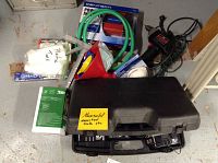 Photo of assorted tools and accessories including tool cases, battery packages, hose, funnels, caulk gun, and face masks arranged on floor
