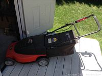 Full side view of the orange and black Black and Decker electric lawn mower with grass catch bag attached, foldable handle visible.