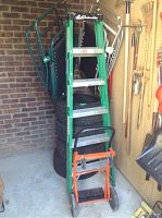 6 ft green Louisville FS4006 ladder with silver steps standing in shed with orange and black Powermaster dolly in front. Tires and chairs visible but excluded.