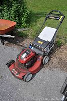 Front perspective showing red deck, Briggs & Stratton engine housing, wheels and grass clippings.
