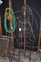 Photo of two garden hoses, three black metal garden trellises approximately 71 inches high, and a yellow power extension lead.