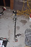 Full view of the Ryobi weed whacker laid on a concrete floor showing length and power head.