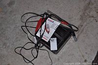 Photo of the battery charger on the ground showing cables and clamps with manual placed on top.