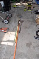 Long shot showing the axe and branch cutter on concrete floor with other garden tools in background