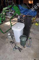 Multiple garden items including lanterns, torch stand, watering can, folding chair and bin arranged indoors in a cluttered space