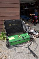 Full view of the John Deere grass catcher with green metal frame, black mesh hamper, adjusted tow bar, and front brush visible