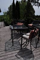 Overview of the patio furniture set on wooden deck showing table and two chairs with cushions from a side angle in daylight