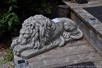 Side view of a detailed solid cement lion statue showing the mane and facial features in relief on a flat base.