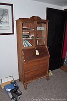 Full view of wooden antique secretary desk with books on shelves and closed drawers.