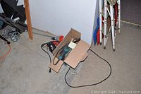 Four power tools tangled with cords on a concrete floor next to wall and folded metal ladders.