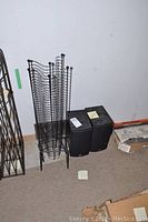 Two black PSB speakers on the floor beside three black metal wire-frame CD stands designed to hold CDs vertically.