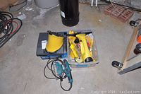 Photo of Makita hand sander, Weller soldering gun, yellow utility knife, low mount mirror, and various other hand tools in plastic bins on concrete floor.