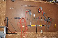 Wall-mounted pegboard displaying various hand tools including a level, wrenches, screwdrivers, hand saws, scissors, measuring tape, clamps, hammer, and an orange extension cord coiled and hung.