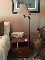 Wood shelf with bottom drawer and Henry Kloss clock radio on top, brass floor lamp next to it.