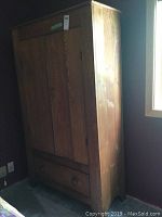 Side view of closed, solid oak armoire showing front drawer and doors