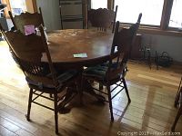 Round wooden kitchen table with four chairs around it, table shows water marks and wear