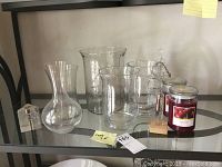 Five varied shapes and sizes of clear glass vases along with a frosted glass Christmas tree, storm gauge on wooden block, two black cherry scented candles, and a small clear glass candle holder.