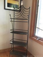 Full view of black metal shelving unit with decorative back, four shelves, located indoors near a window and framed artwork.